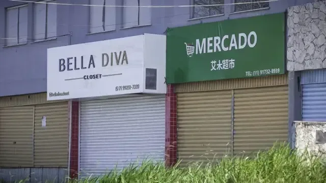 Imagem de rua comercial em Camaçari mostra loja "Bella Diva" ao lado de um mercado chinês, com ideogramas na fachada