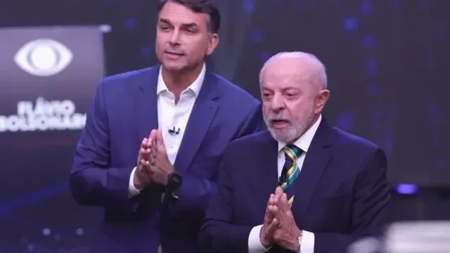 Flávio Bolsonaro e Lula em posições semelhantes, com mãos unidas em forma de oração, fotografados durante o debate nos estúdios da Band